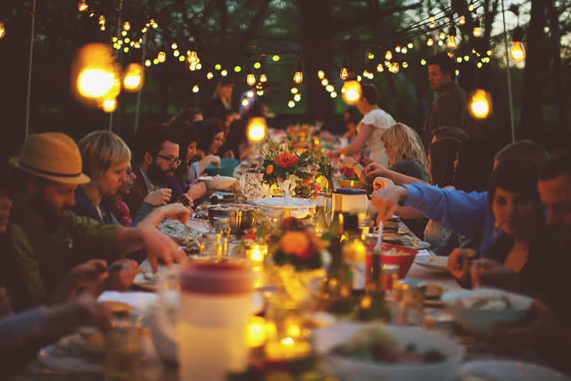 A long candlelit table under string lights at night