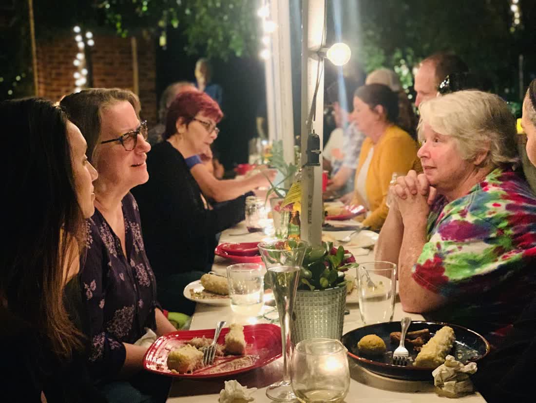Neighbors in conversation at a long candlelit community table